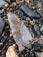 Photograph of pre-European projectile point stone tool lying on pebble shore