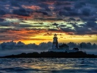 Photo ambiante du phare de Head Harbour à l’aube devant un ciel orange vif et des bancs de nuages en arrière-plan.