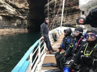 Photograph of three SCUBA divers on vessel deck with sea cave in the background.